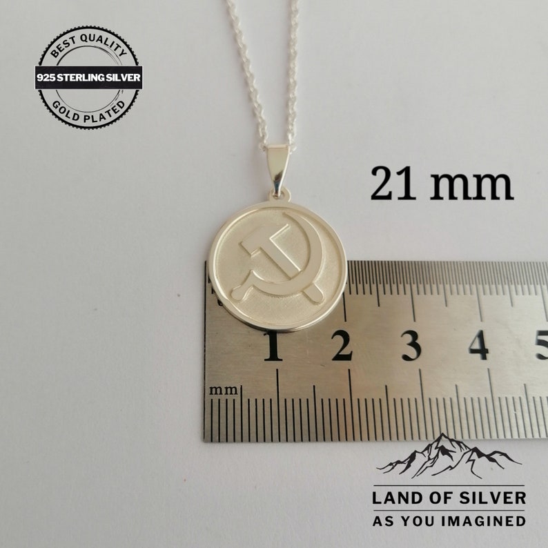 May include: Silver pendant necklace featuring a 21 mm round charm with a hammer and sickle design. The charm is gold plated and has the text "BEST QUALITY 925 STERLING SILVER GOLD PLATED" on the back. The necklace is on a silver chain.