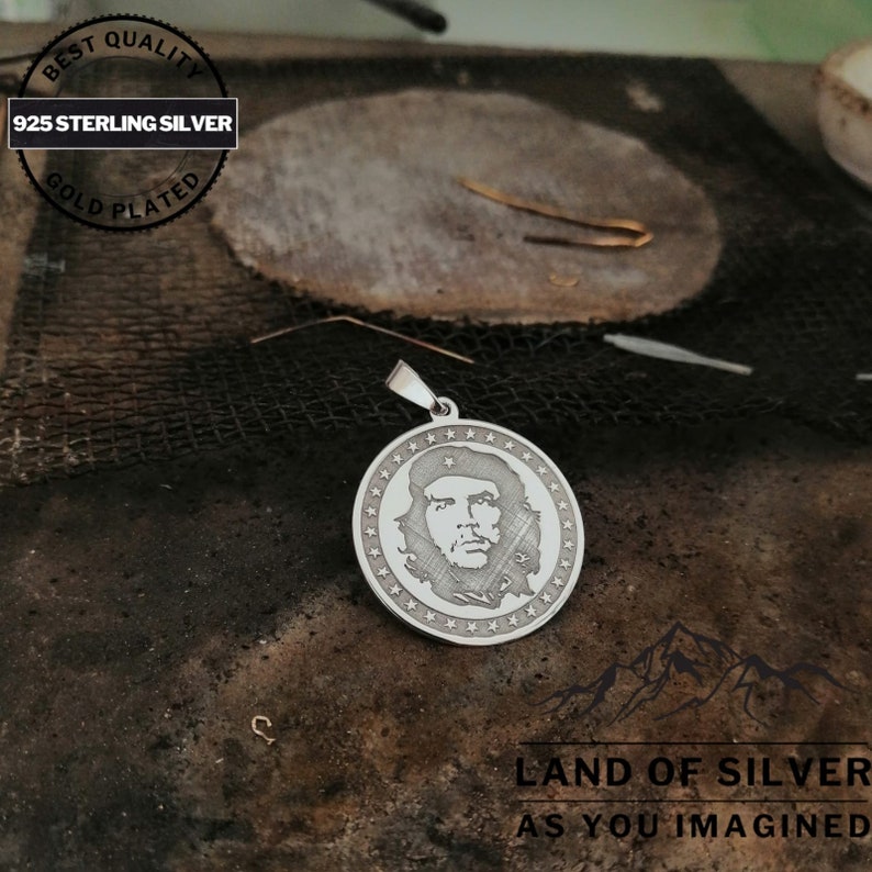 May include: A silver pendant featuring a portrait of Che Guevara, surrounded by a circle of stars. The pendant is made of 925 sterling silver and is gold plated. The text "BEST QUALITY 925 STERLING SILVER GOLD PLATED" is visible on the top of the image. The text "LAND OF SILVER AS YOU IMAGINED" is visible at the bottom of the image.