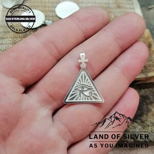 May include: Silver pendant featuring a triangle with an eye inside, surrounded by rays. The pendant is attached to a small cross. The pendant is made of 925 sterling silver and is gold plated. The text "BEST QUALITY 925 STERLING SILVER GOLD PLATED" is visible on the image.