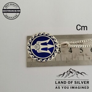 May include: A silver pendant with a blue enamel design of a trident, a traditional symbol of Ukraine, surrounded by a wave pattern. The pendant is 3 cm in diameter and is shown on a ruler for size reference.