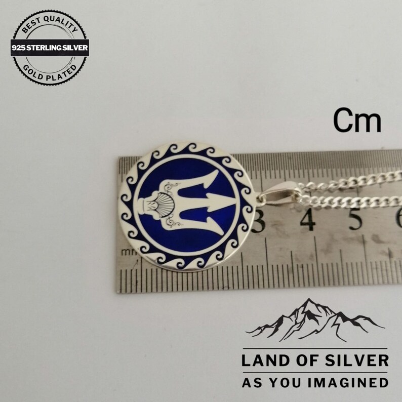 May include: A silver pendant with a blue enamel design of a trident, a traditional symbol of Ukraine, surrounded by a wave pattern. The pendant is 3 cm in diameter and is shown on a ruler for size reference.