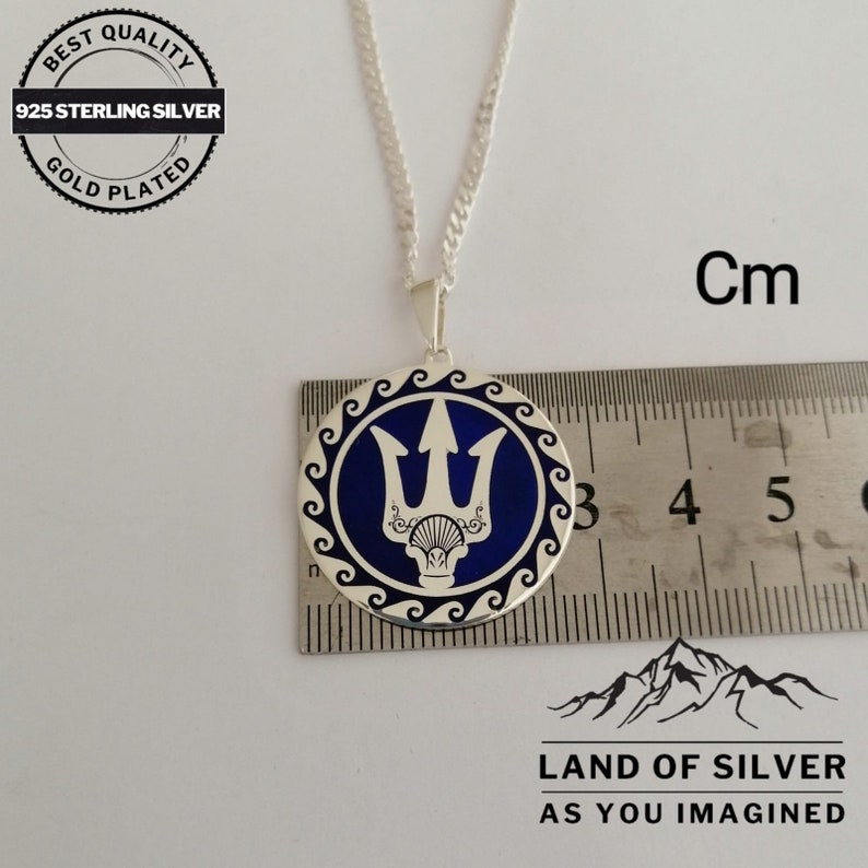 May include: A silver necklace with a round pendant featuring a blue enamel trident design. The pendant is approximately 2.5 cm in diameter. The necklace is 925 sterling silver and gold plated.