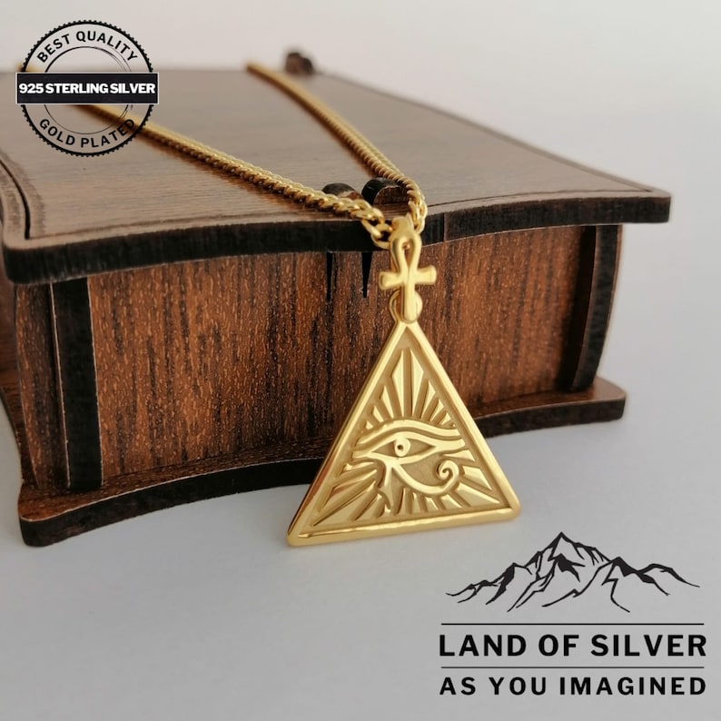 A customizable, gold-plated 925 sterling silver necklace featuring the Eye of Horus. The pendant has a triangular design containing an eye, with a small Ankh symbol at the top.