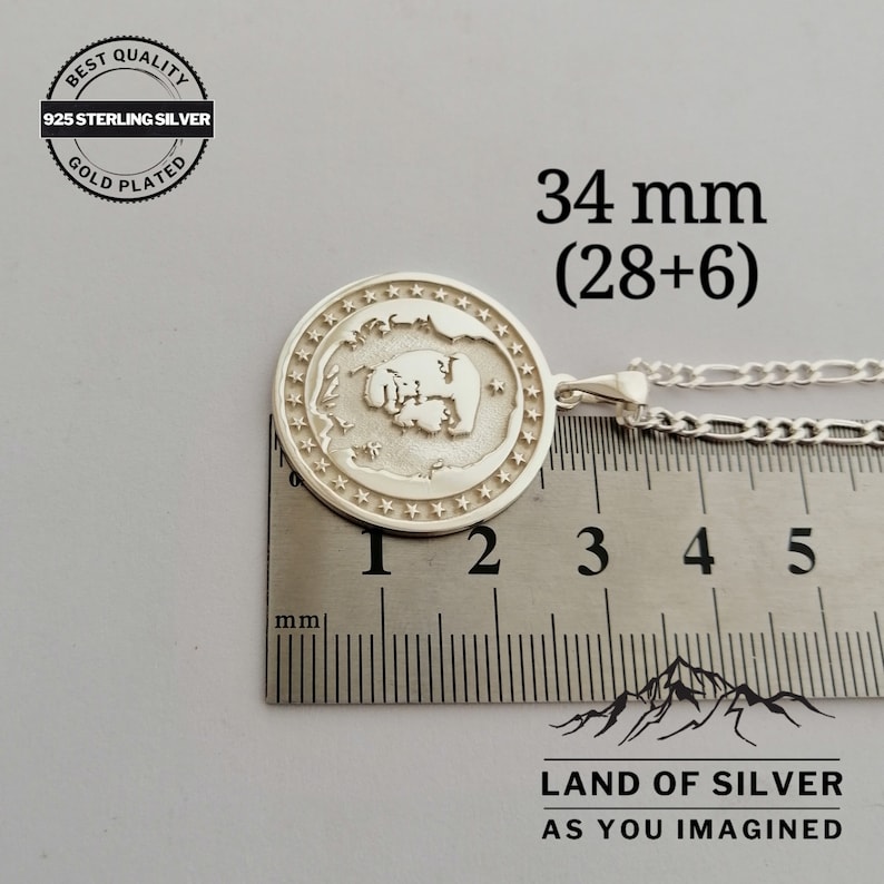 May include: A silver pendant with a detailed design of a fist, surrounded by stars, on a silver chain. The pendant measures 34 mm (28+6) in diameter. The pendant is on a ruler for size reference. The pendant is labeled "BEST QUALITY 925 STERLING SILVER GOLD PLATED" and "LAND OF SILVER AS YOU IMAGINED".