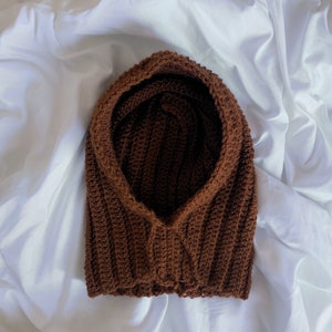 May include: A brown crocheted hooded cowl, lying on a white surface.