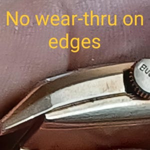 K&ouml;nnte beinhalten: Nahaufnahme eines silbernen Uhrenarmbands mit dem Wort "BULOVA" an der Seite. Das Armband weist keine Abnutzung an den Kanten auf. "No wear-thru on edges" ist in gelber Schrift auf braunem Hintergrund geschrieben.