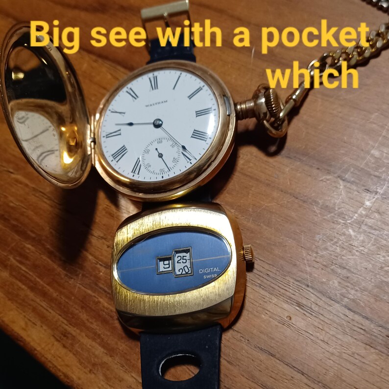 Puede incluir: Un reloj de bolsillo dorado con esfera blanca y n&uacute;meros romanos negros, abierto para mostrar la hora. Debajo, un reloj digital dorado con esfera azul muestra la fecha. El texto "Big see with a pocket which" es visible.