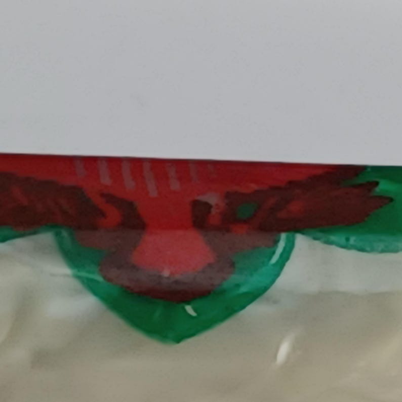 May include: A red and green painted design featuring a bird-like shape with outstretched wings. The design is set against a white background, with the bird shape in the center of a green, heart-like shape.