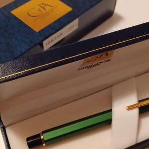 Puede incluir: Una pluma estilogr&aacute;fica verde y dorada en una caja azul con el texto "2/1 CAMISADO" en el interior de la tapa de la caja.