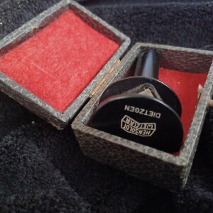 May include: A vintage black Hensoldt Wetzlar Dieztgen optical instrument in a textured case with a red velvet interior. The case is open, revealing the instrument and its components.