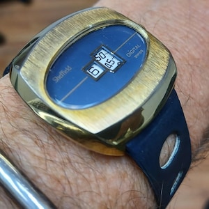 Puede incluir: Un reloj digital Sheffield vintage con caja dorada y esfera azul. El reloj muestra la hora con n&uacute;meros digitales. El reloj tiene una correa azul oscuro. Las palabras "Sheffield" y "DIGITAL SWISS" son visibles en la esfera.