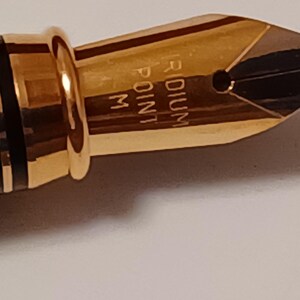 Puede incluir: Primer plano de una plumilla de pluma dorada con la inscripci&oacute;n "Iridium Point M".