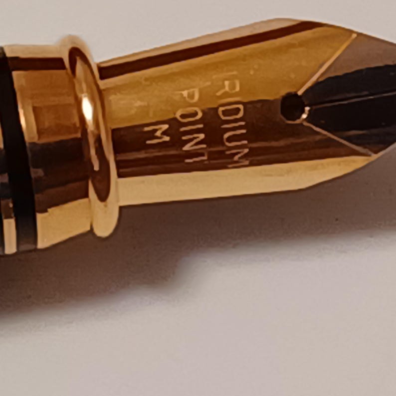 Puede incluir: Primer plano de una plumilla de pluma dorada con la inscripci&oacute;n "Iridium Point M".