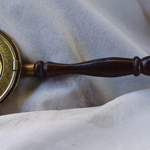 May include: A brass clock with a wooden handle. The clock face has Roman numerals and the words "The British Time" printed on the face.