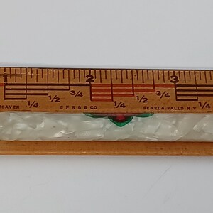 May include: A vintage mechanical pencil with a pearlescent white barrel and silver accents. The pencil has a decorative design with red and green details. It is placed next to a wooden ruler.