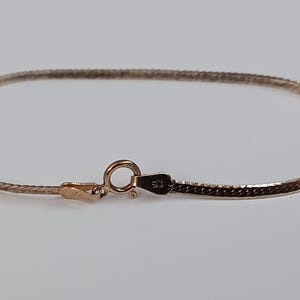 May include: A gold-toned chain bracelet with a delicate, braided design. The bracelet has a simple clasp closure.
