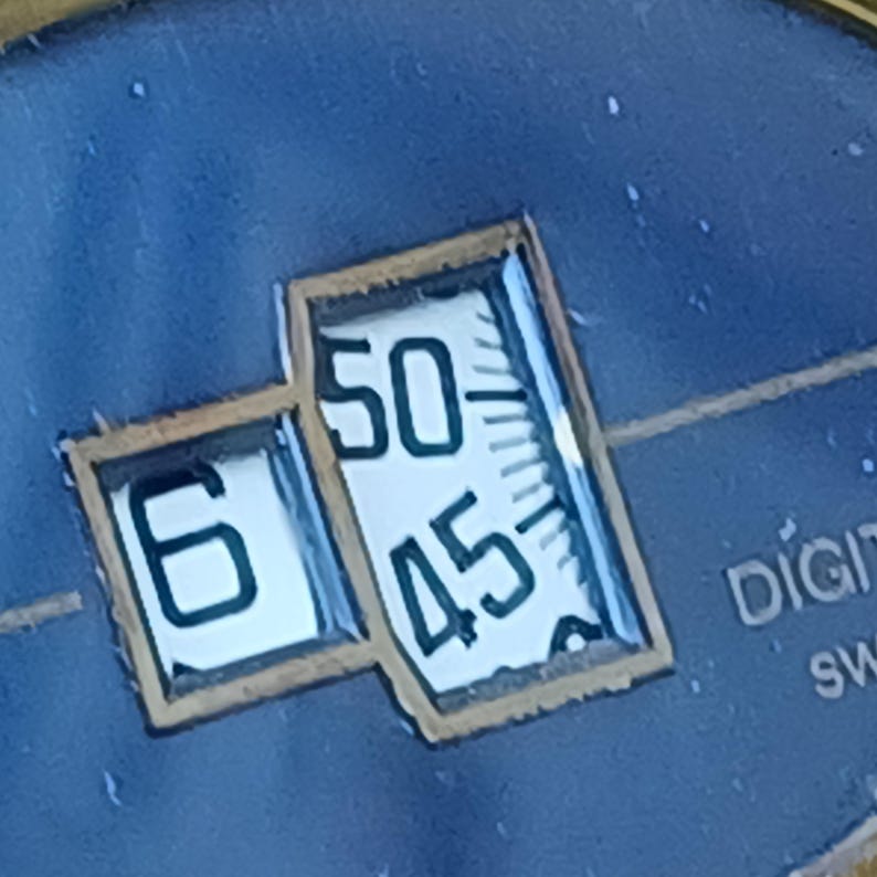 Puede incluir: Primer plano de una esfera de reloj con una pantalla digital que muestra la hora. La pantalla muestra el n&uacute;mero 6 y los n&uacute;meros 50 y 45. El fondo es de color azul oscuro.