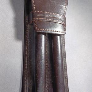 May include: A brown leather pen case with the "HONDA" logo embossed on the top flap. The case has a stitched design and a strap closure. The case appears to be designed to hold multiple pens.