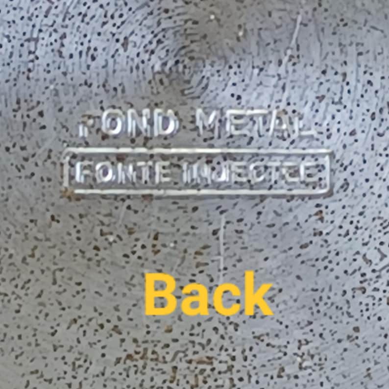 May include: Close-up of a textured, silver-colored metal surface. The words "POND METAL" are stamped at the top, with "FONTE INJECTEE" below. The word "Back" is written in yellow at the bottom.