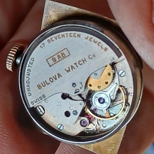 K&ouml;nnte beinhalten: Die R&uuml;ckseite einer silbernen Bulova-Uhr mit einem 17-Steine-Werk. Die Uhr ist mit "Bulova Watch Co. Swiss" und "17 Seventeen Jewels" beschriftet und hat die Seriennummer "9 AB".