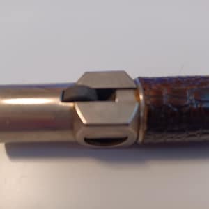 May include: A cylindrical lighter featuring a metallic silver finish on the ignition end with a small textured black thumb wheel. The body of the lighter is wrapped in a dark brown material with a raised, embossed crocodile skin texture pattern.