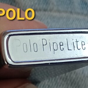 May include: A rectangular silver-toned metal lighter with rounded edges. The bottom surface is engraved with the text 'Polo Pipe Lite' and 'JAPAN'. The word 'POLO' is also displayed in yellow text in the upper left corner of the image.