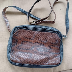 May include: A brown and black snakeskin shoulder bag with a black leather strap. The bag has a zipper closure and a flap.