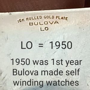 K&ouml;nnte beinhalten: Nahaufnahme einer Uhreninschrift mit der Aufschrift "10K Rolled Gold Plate Bulova LO" und "LO = 1950". Die Inschrift lautet weiter: "1950 was 1st year Bulova made self winding watches."
