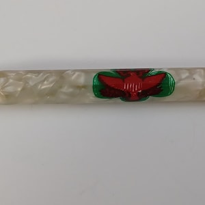May include: A vintage pen with a pearlescent white barrel and a silver tip. The pen features a red and green emblem. A small metal loop is attached to the end of the pen.