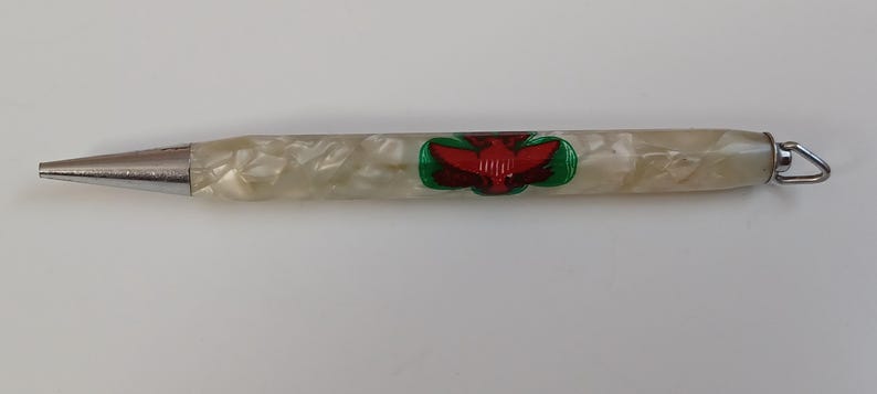 May include: A vintage pen with a pearlescent white barrel and a silver tip. The pen features a red and green emblem. A small metal loop is attached to the end of the pen.