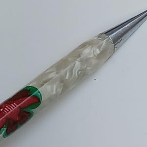 May include: A knitting needle with a silver tip and a handle featuring a white, marbled design. The base of the handle has a red and green floral pattern. The needle is designed for crafting.
