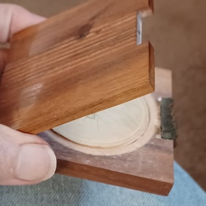 May include: A wooden box with a hinged lid, the lid is open revealing a white circular object inside.