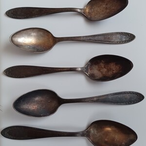 May include: Five silver spoons with tarnished surfaces. The spoons are arranged vertically in a row, with the handles pointing to the right.