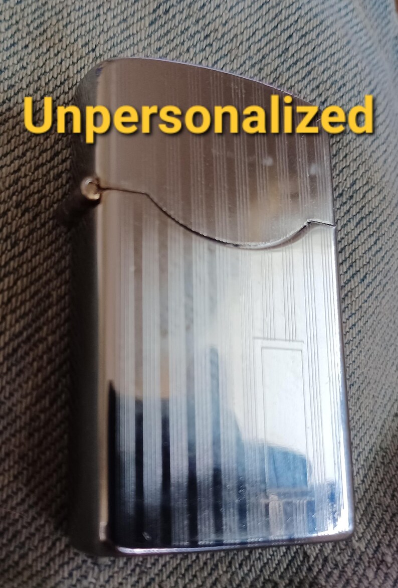 May include: A rectangular silver-tone metal lighter with a hinged lid and a vertical striped pattern. The word Unpersonalized is printed in yellow text across the top portion of the lighter. The surface is reflective with a smooth metallic finish.