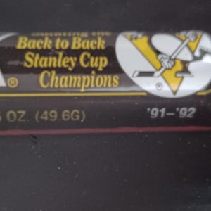 May include: A black and gold image with text that reads "Back to Back Stanley Cup Champions." The image also includes the Pittsburgh Penguins logo and the years '91-'92. The text also includes the measurement of 5 OZ. (49.6G).