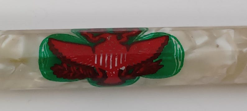 May include: A clear, rectangular pen with a white, pearlescent finish. The pen features a red eagle emblem with green and white accents. The eagle is centered on the pen's barrel.