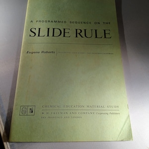 May include: A green book cover with the title "A Programmed Sequence on the Slide Rule" by Eugene Roberts, Polytechnic High School, San Francisco, California. The book is published by W.H. Freeman and Company, Cooperating Publishers, San Francisco and London.
