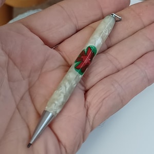 May include: A vintage mechanical pencil with a pearlescent white barrel and a silver tip. The barrel features a red and green floral design. A small silver loop is attached to the top of the pencil.