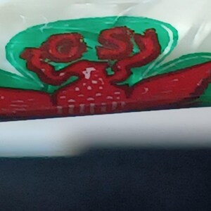 May include: A close-up of a package with a red and white illustration. The illustration features a red creature with the letters "OS" in red. The creature is set against a green background.
