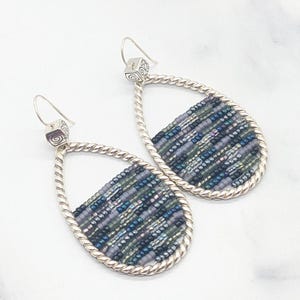 May include: Teardrop-shaped earrings with a silver twisted rope design. The earrings feature a beaded section with shades of blue, green, and purple. The ear hooks have a small square design with a spiral detail. A stylish accessory.