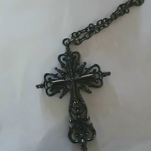 May include: A black metal cross pendant necklace with a detailed, ornate design. The cross is attached to a black chain.