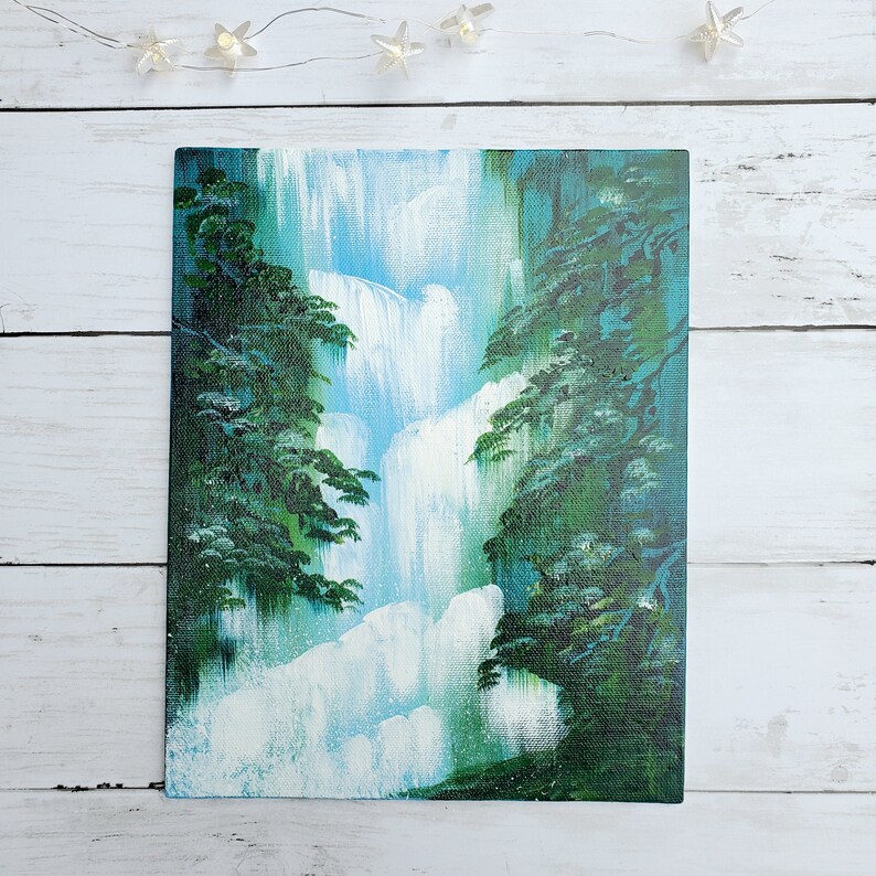 May include: A painting of a waterfall cascading down a cliffside, surrounded by lush green trees. The water is painted in shades of blue and white, while the trees are a deep green.