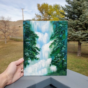 May include: A painting of a waterfall cascading down a cliff, framed by lush green trees. The painting is done in a realistic style with a focus on the water's movement and the trees' foliage.