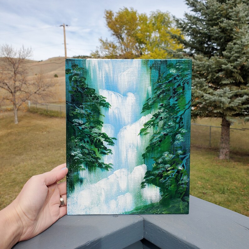 May include: A painting of a waterfall cascading down a cliff, framed by lush green trees. The painting is done in a realistic style with a focus on the water's movement and the trees' foliage.