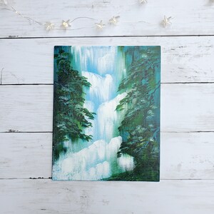 May include: A painting of a waterfall cascading down a cliff face, surrounded by lush green trees. The water is a light blue and white, and the trees are a deep green.