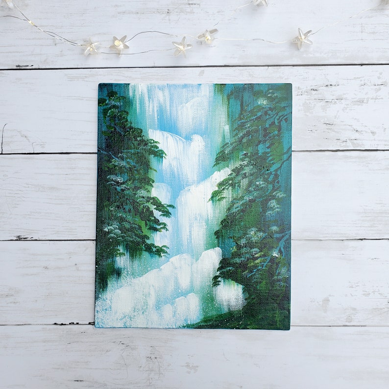 May include: A painting of a waterfall cascading down a cliff face, surrounded by lush green trees. The water is a light blue and white, and the trees are a deep green.