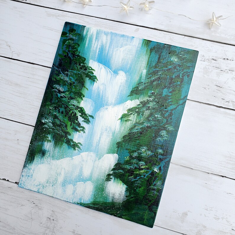 May include: A painting of a waterfall cascading down a rocky cliff, surrounded by lush green trees. The water is white and blue, and the trees are a deep green.