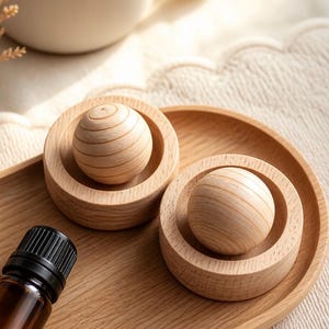 May include: Two wooden aromatherapy diffusers with a spherical design, each set within a circular base. The wood grain is visible. A brown essential oil bottle with a black cap is in the foreground, suggesting a wellness theme.