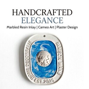 Puede incluir: Una placa ovalada de yeso con una incrustación de resina veteada en azul y blanco y un relieve central de camafeo con un perfil. El borde incluye el texto HANDCRAFTED ELEGANCE, Marbled Resin Inlay | Cameo Art | Plaster Design, HOME DECORRALIE, MAISON MANE y EST. 2025.