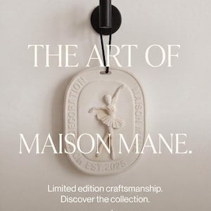 May include: An oval-shaped off-white wall plaque featuring a relief of a ballet dancer in a tutu. The plaque is suspended by a black cord from a black cylindrical wall hook. Text on the plaque reads DECORATION MAISON MANE EST. 2025.